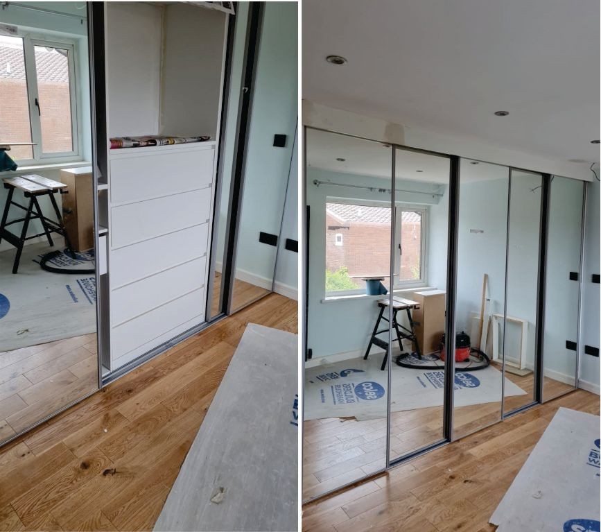 A room under renovation with partially installed mirrored sliding wardrobe doors and a window in the background.