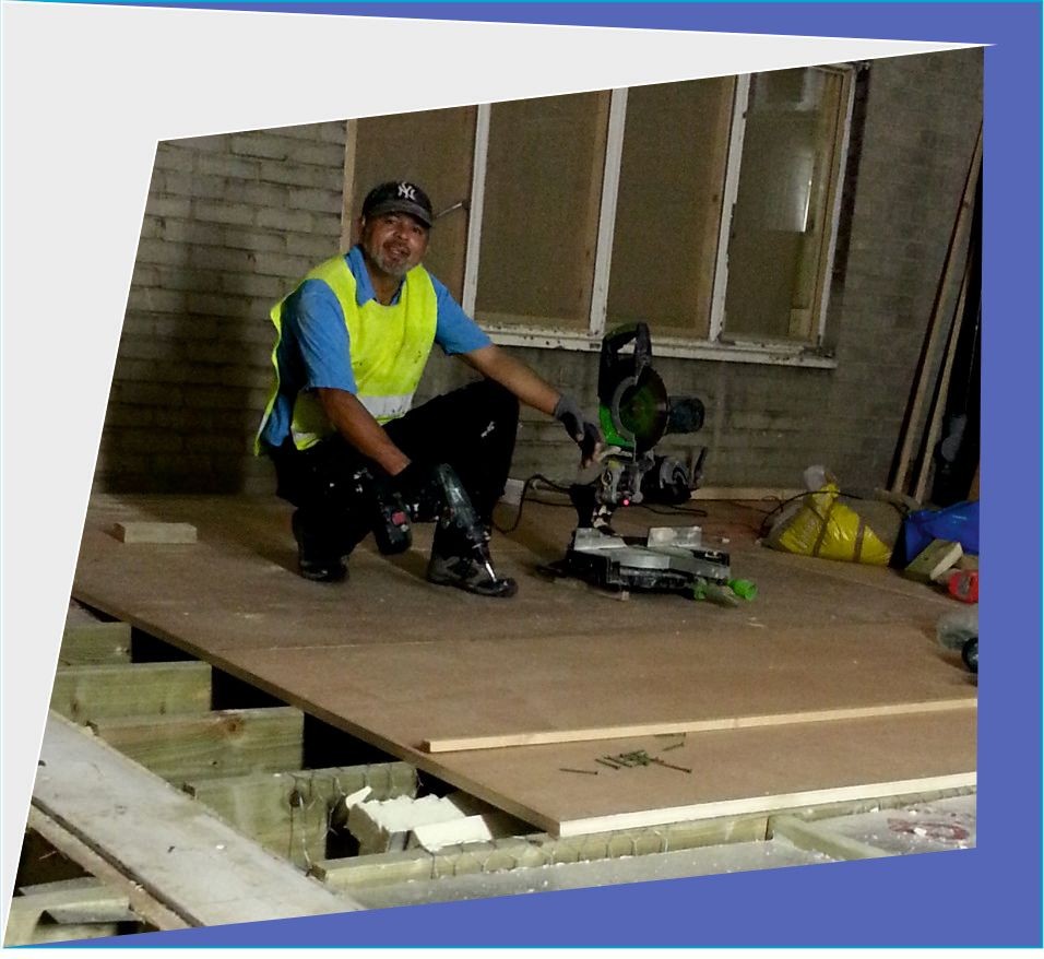 Construction worker kneeling on a wooden platform with a circular saw and other construction materials around.