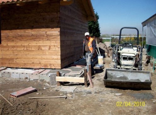 Construction site with a worker in a safety vest standing beside an unfinished building and construction equipment.