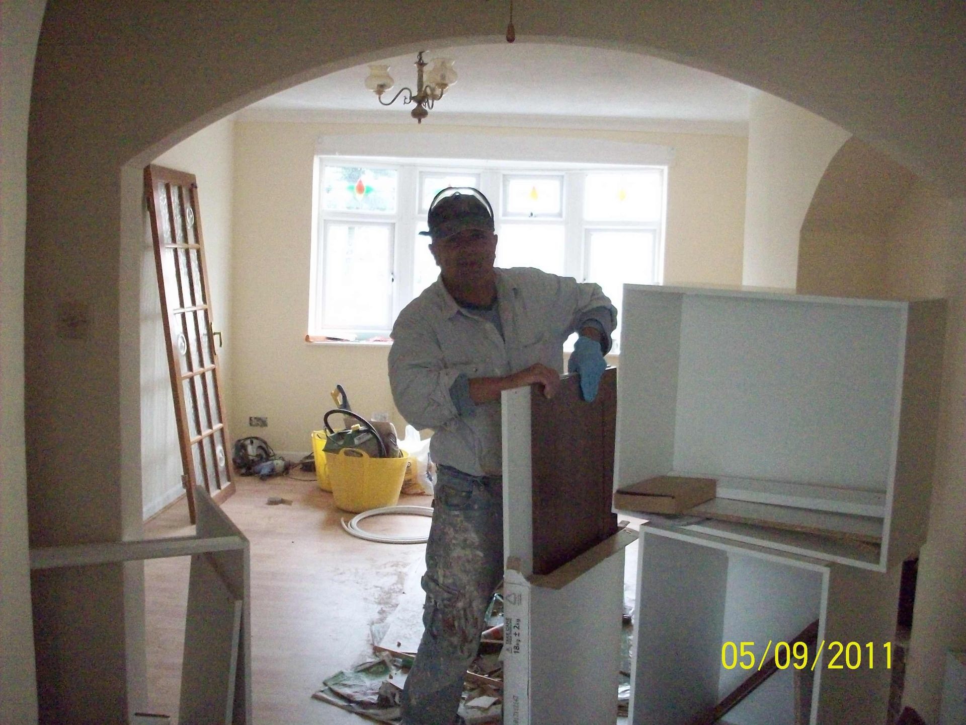 Person assembling white furniture in a room under renovation, with tools and materials scattered around.